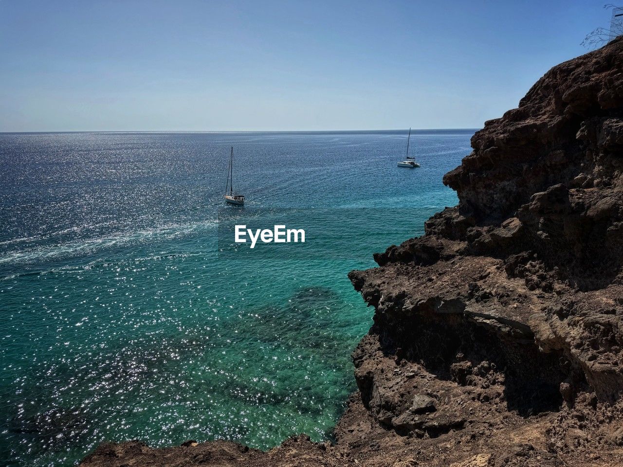 water, sea, sky, scenics - nature, beauty in nature, ocean, land, coast, nature, nautical vessel, horizon over water, shore, horizon, beach, body of water, rock, cliff, terrain, transportation, blue, tranquil scene, tranquility, travel, mode of transportation, bay, day, clear sky, travel destinations, outdoors, idyllic, non-urban scene, sailboat, no people, rock formation, holiday, coastline, vacation, trip, cove, wave, tourism, sunlight, seascape, sailing, motion, sunny