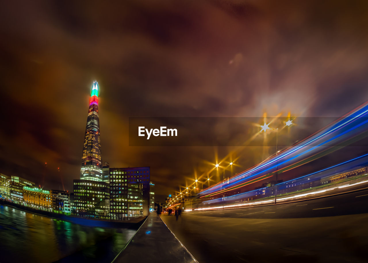 Light trails on bridge over thames river by illuminated the shard against sky at night