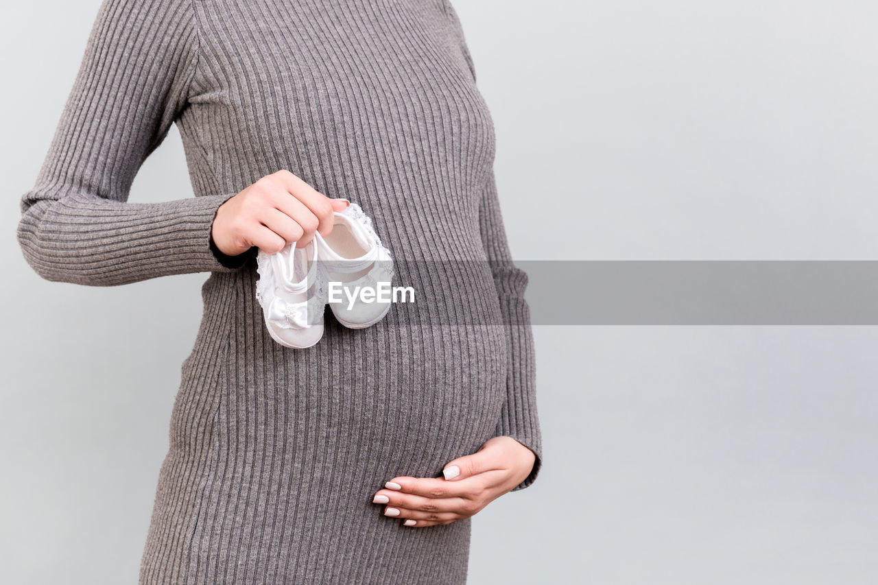 MIDSECTION OF WOMAN HOLDING CAMERA AGAINST WHITE BACKGROUND