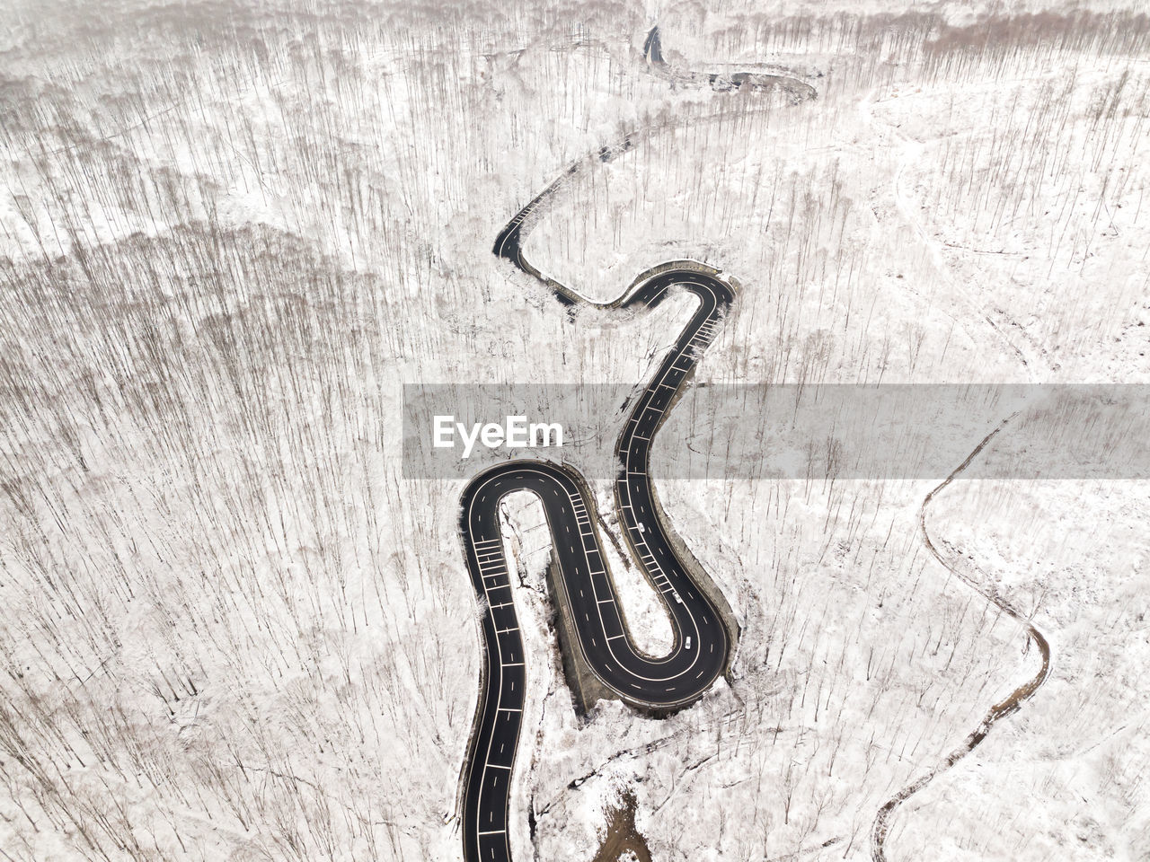 Curvy windy road in snow covered forest, top down aerial view.