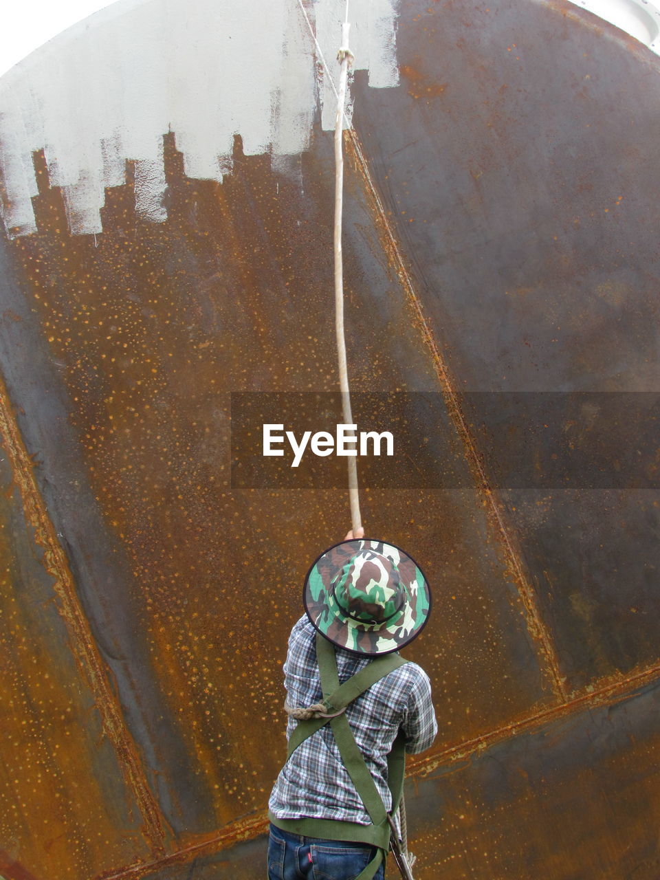 Rear view of man painting rusty metallic wall