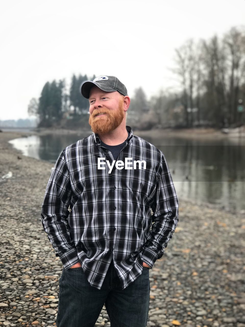 Smiling bearded man looking away while standing against lake