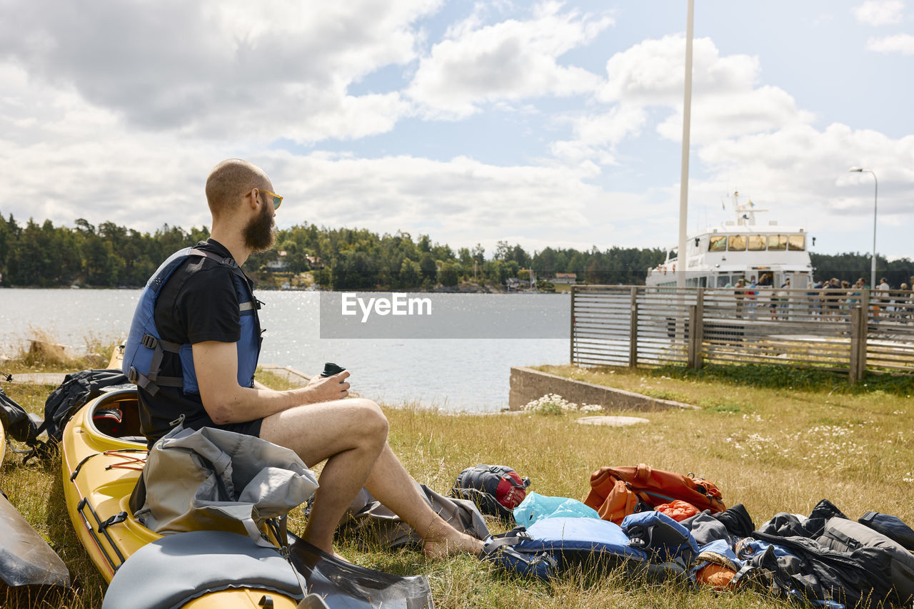 Man sitting on kayak and looking at people boarding ferry