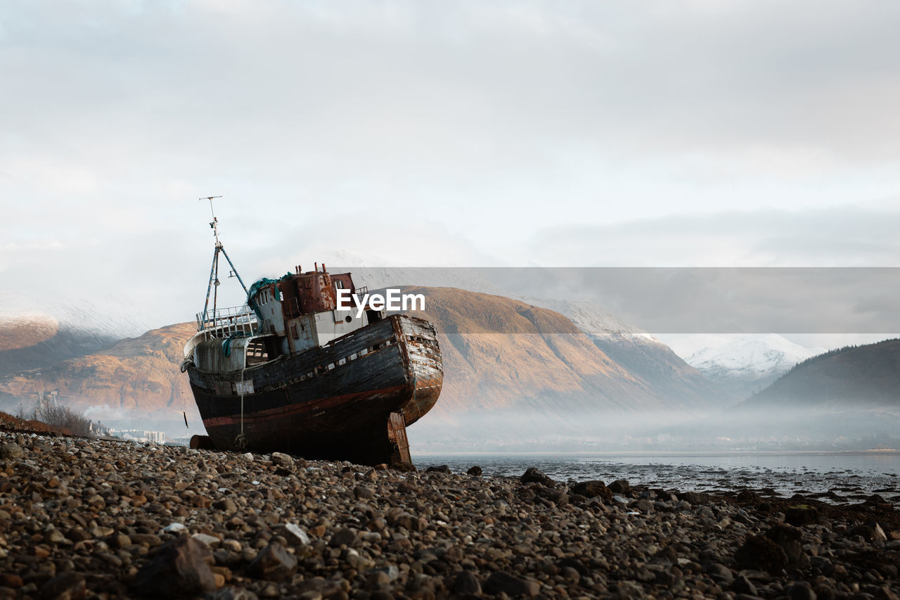 Old rusty fishing boat moored on beach in foggy morning in scottish highlands