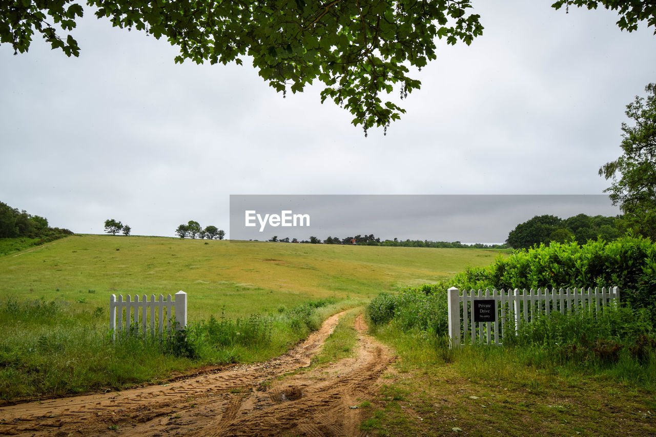 Road passing through field against cloudy sky