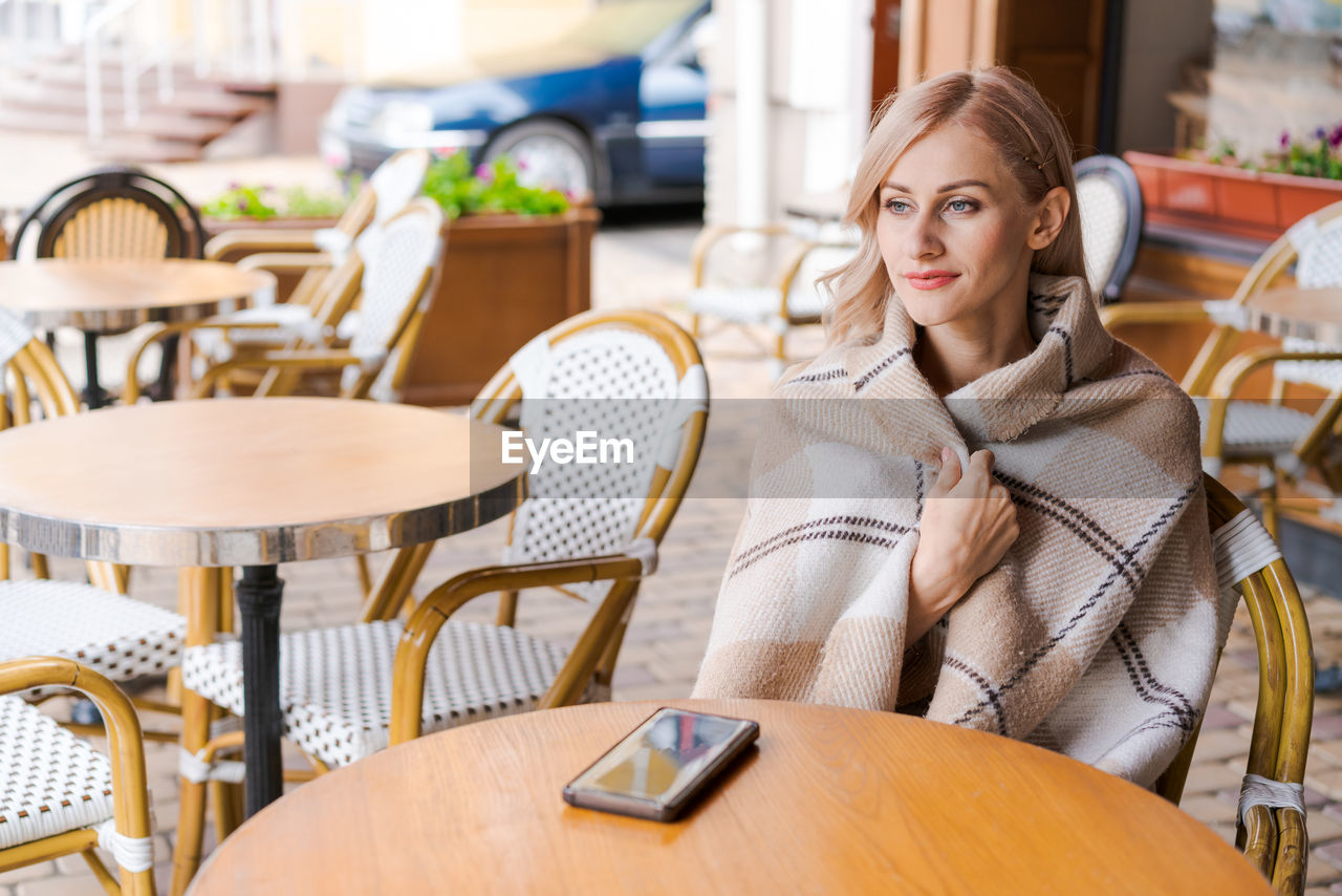 Young beautiful woman, in cafe, drinking coffee in cup, in cozy plaid happy