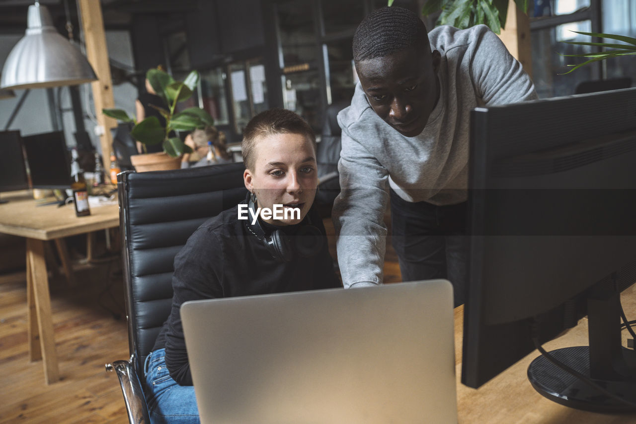 Computer programmer by female coworker using laptop at workplace