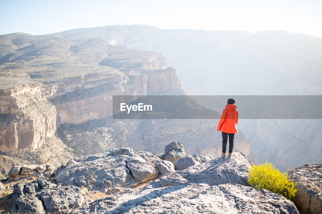 Rear view of woman standing on rock against sky