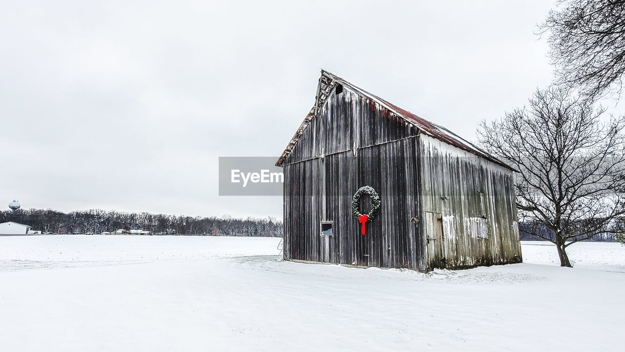 HOUSE ON SNOW COVERED FIELD BY BUILDING AGAINST SKY