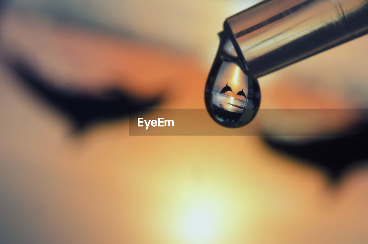 Close-up of water drop against sky at sunset