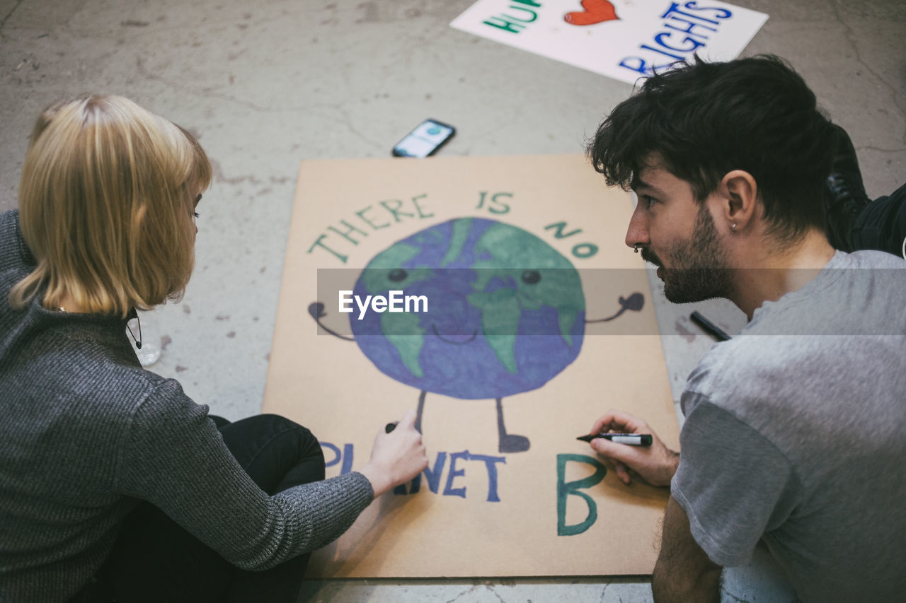 Young male and female protestor preparing poster for environmental issues