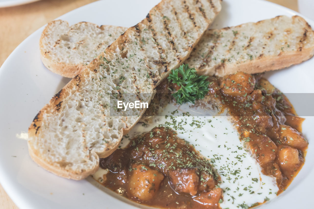 High angle view of beef goulash with toasted bread in plate on table