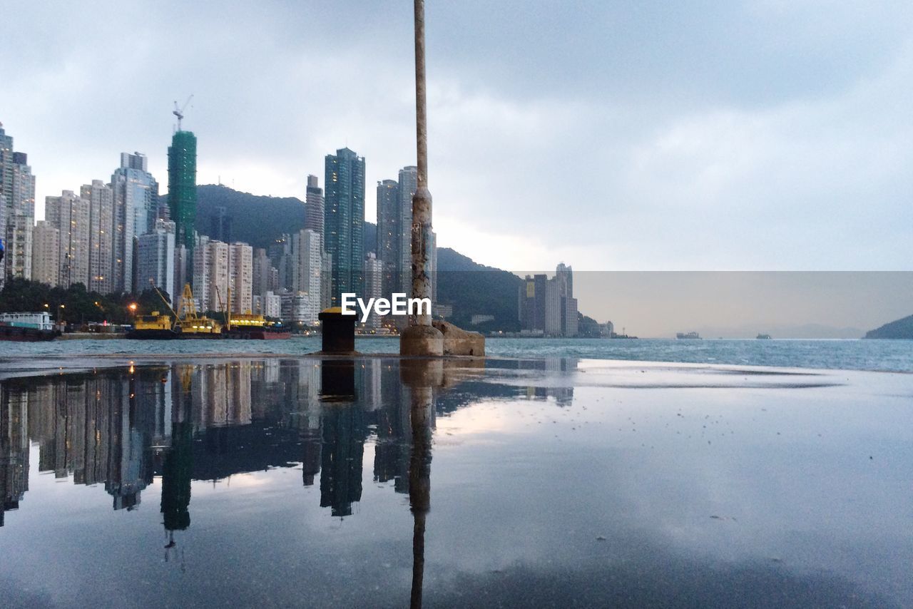 View of city at waterfront against cloudy sky