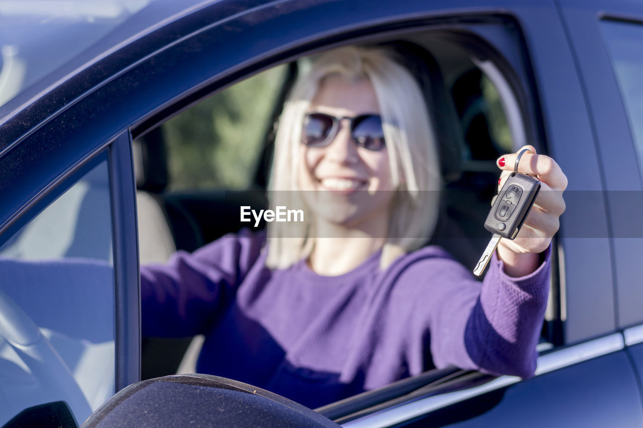 Portrait of smiling woman holding key while sitting in car