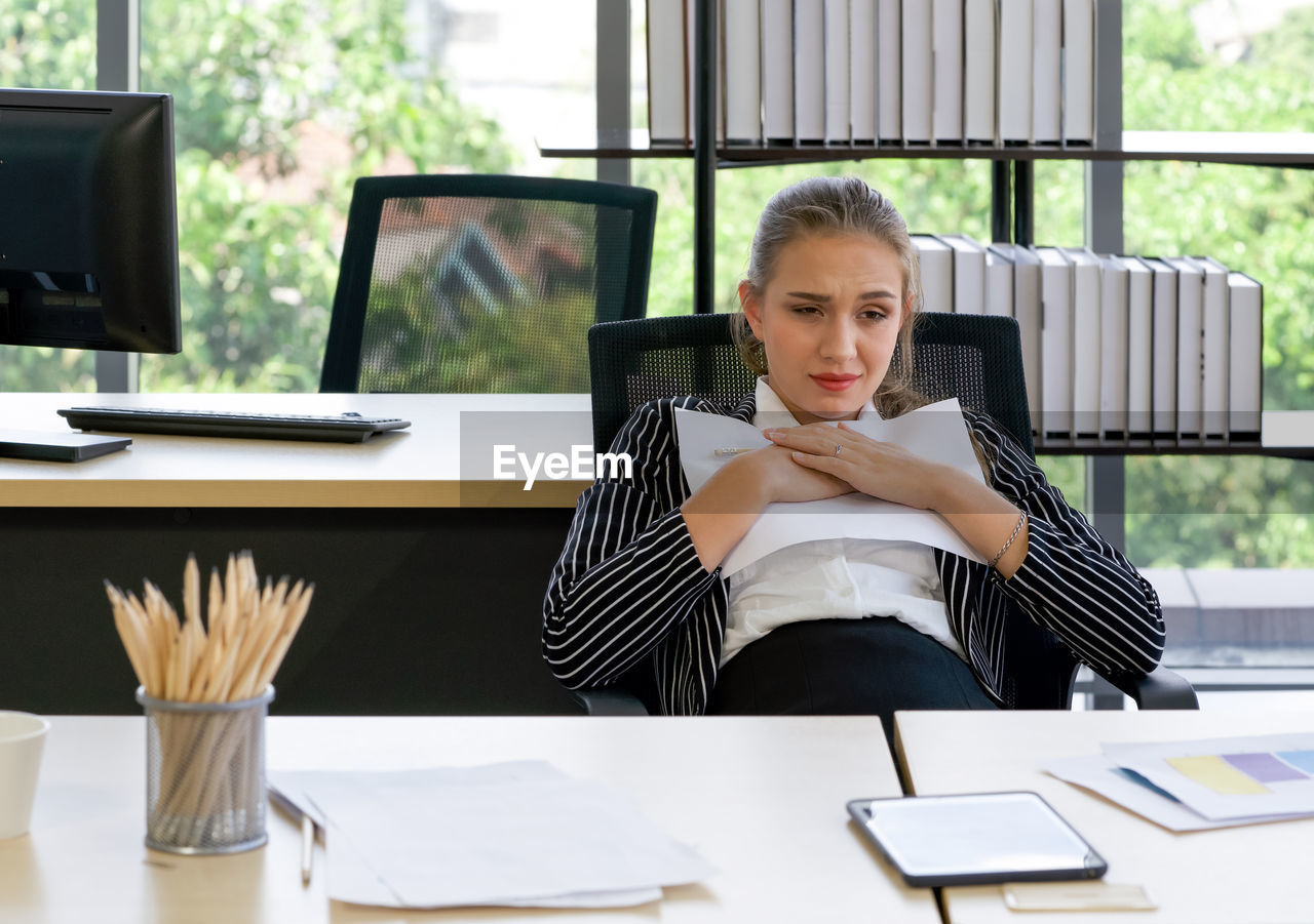 Sad caucasian businesswoman losing job, sitting on the table in the office. 