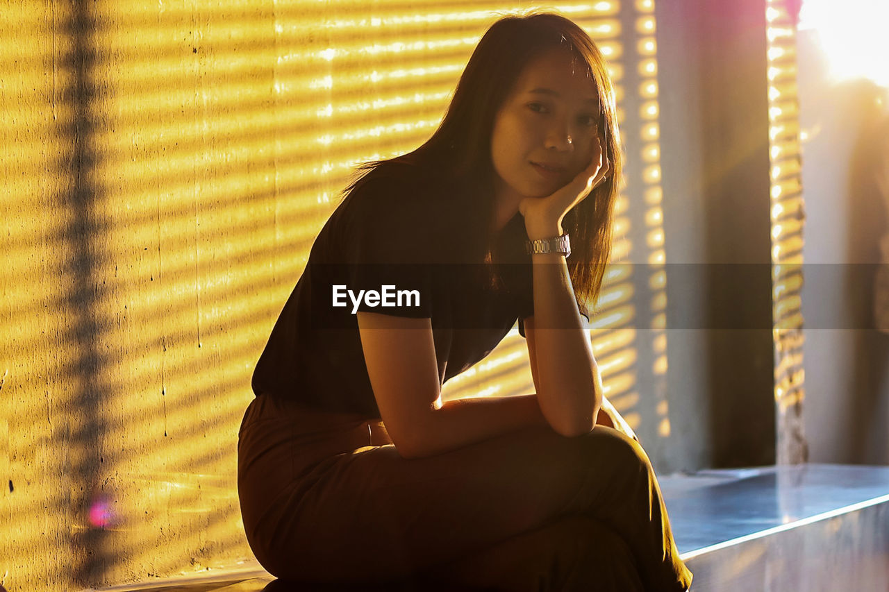 Portrait of young woman sitting in city during sunset