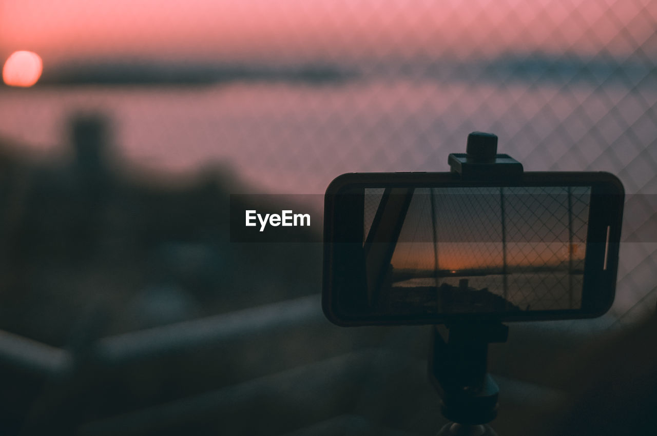 Close-up of smartphone photographing against sky at sunset