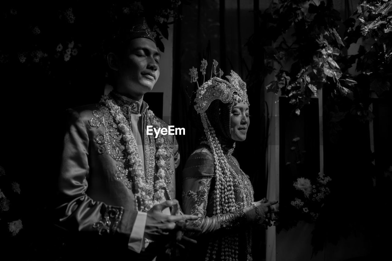 Couples looking away while standing against plants