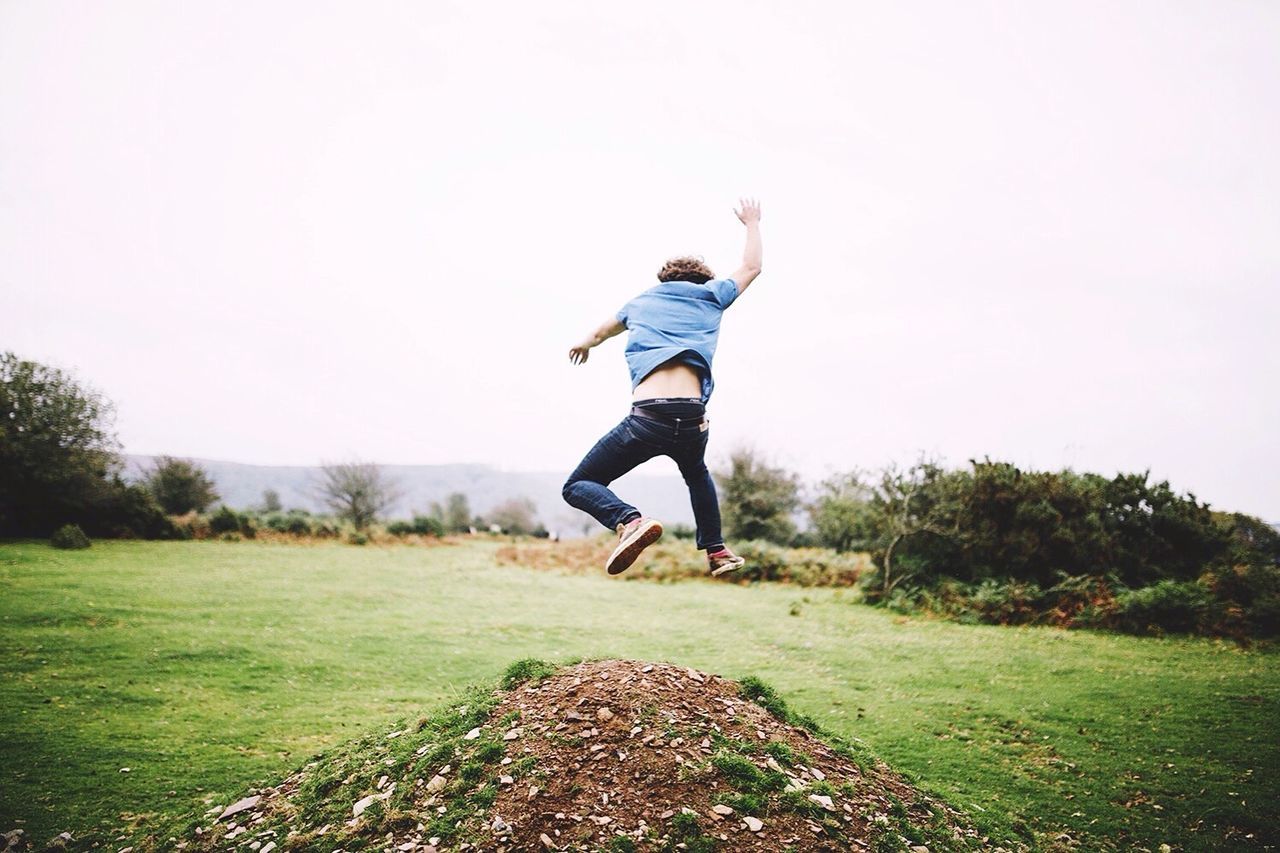 Rear view of excited man jumping over field against sky