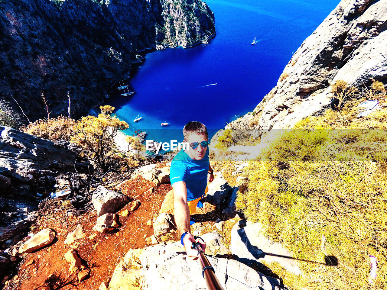 HIGH ANGLE VIEW OF MAN STANDING ON ROCK AGAINST SEA