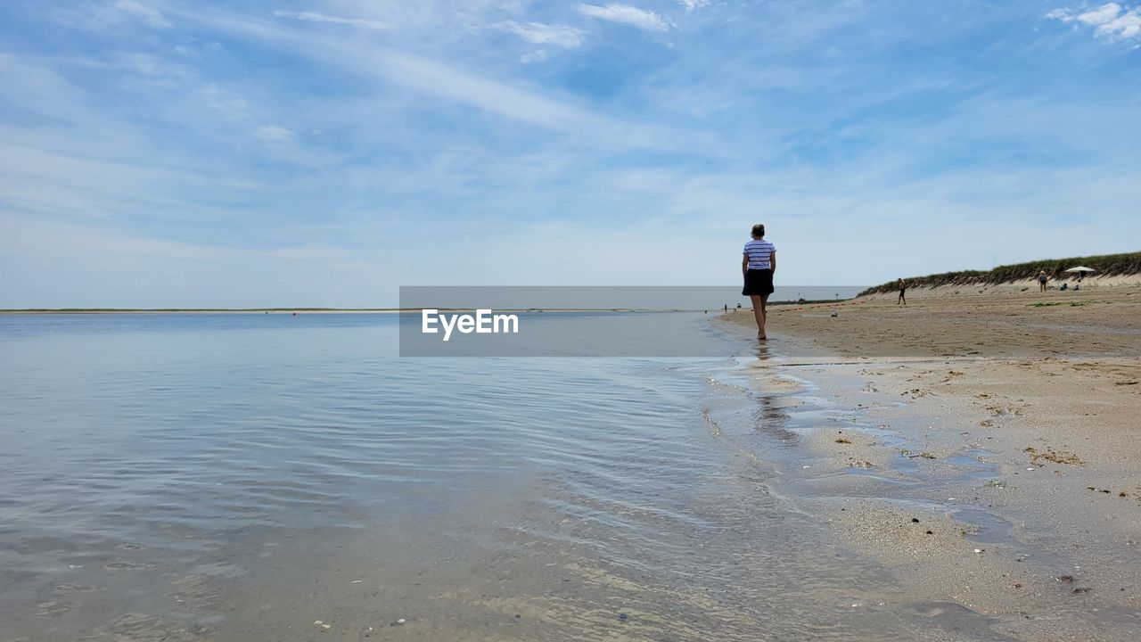 REAR VIEW OF PERSON ON BEACH AGAINST SKY