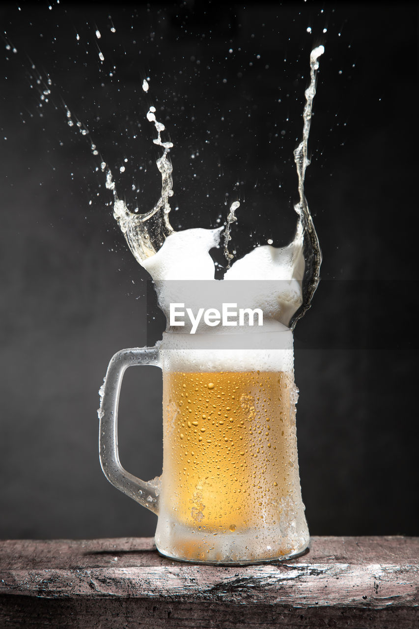 Mug of beer with foam and splashes on wooden table isolated on dark background. vertical format.