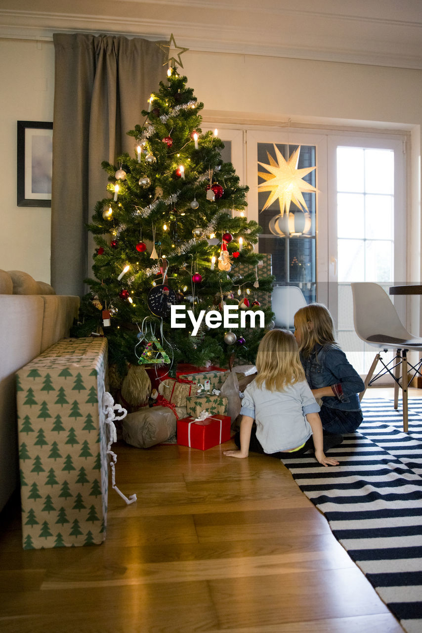 Girls sitting in front of christmas tree