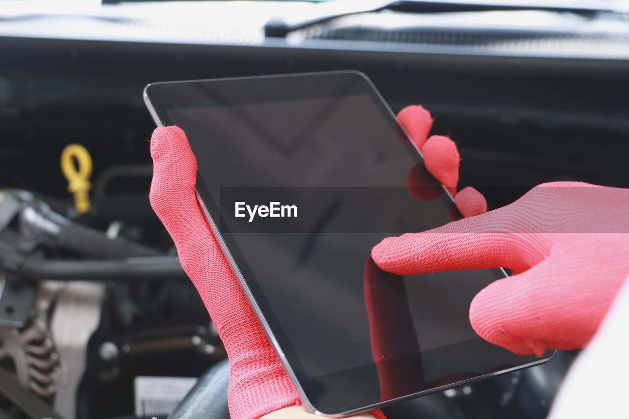 Cropped hands of mechanic using digital tablet against car engine