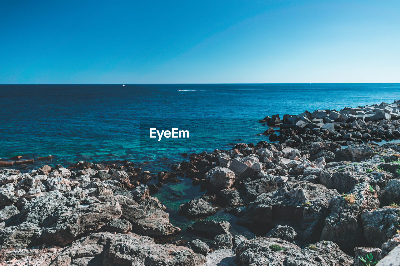 ROCKS BY SEA AGAINST CLEAR BLUE SKY