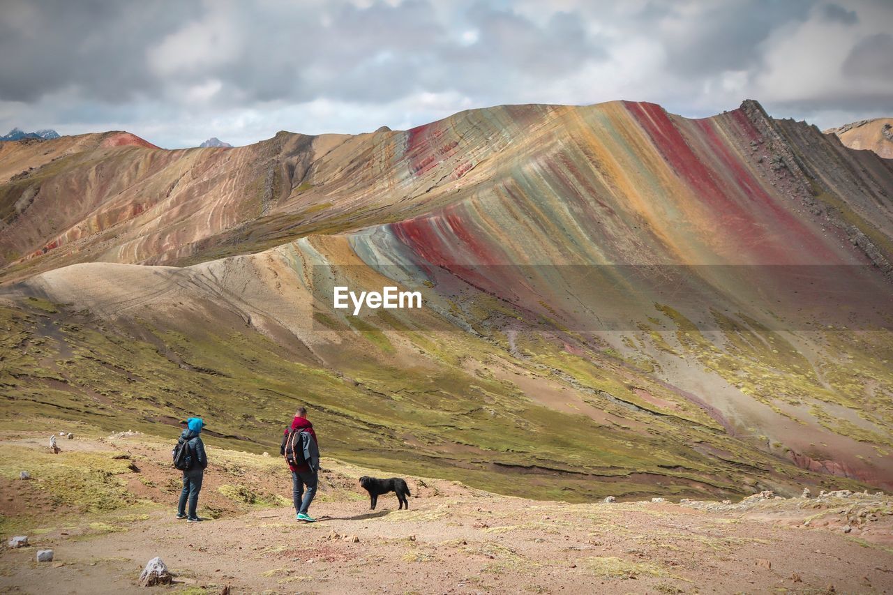 Rear view of people by dog on land against mountain and sky