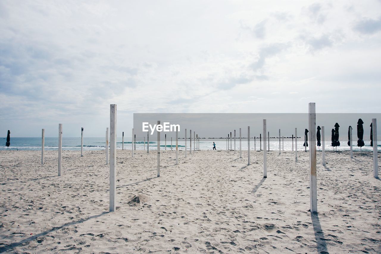 Poles on shore at beach against cloudy sky