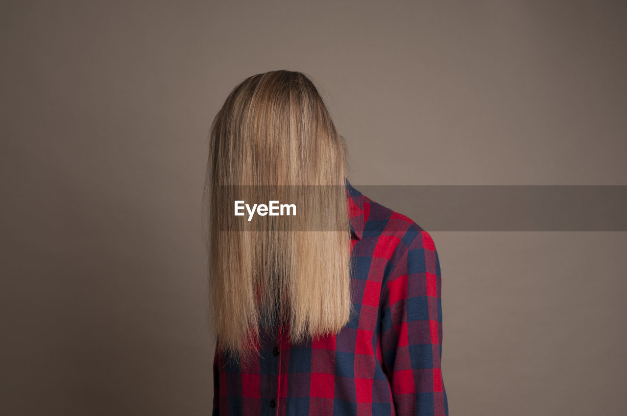 Woman covering face with hair against brown background