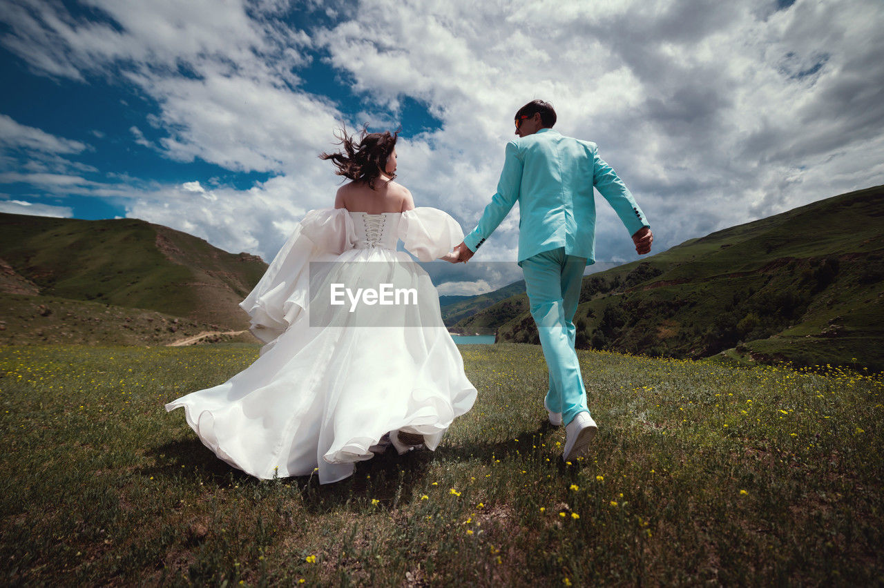 Wedding couple runs. happy man and woman running through a field in the mountains after a wedding