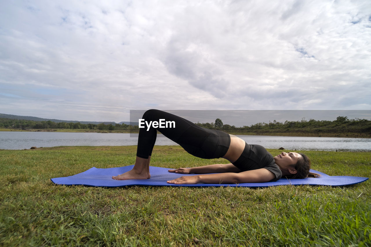 Asian woman in exercise clothes doing yoga poses outdoors in bridge pose. on a yoga mat.