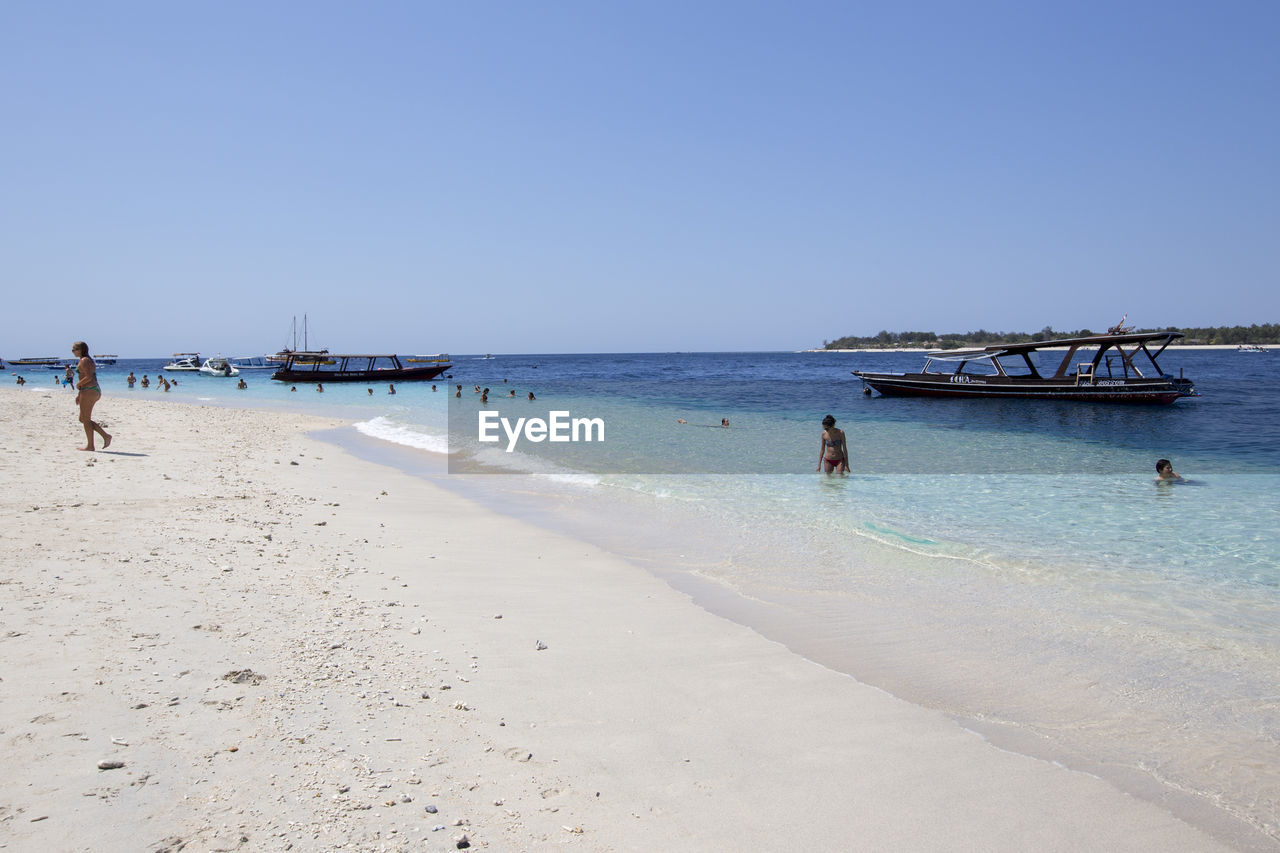 PEOPLE ENJOYING ON BEACH AGAINST CLEAR SKY