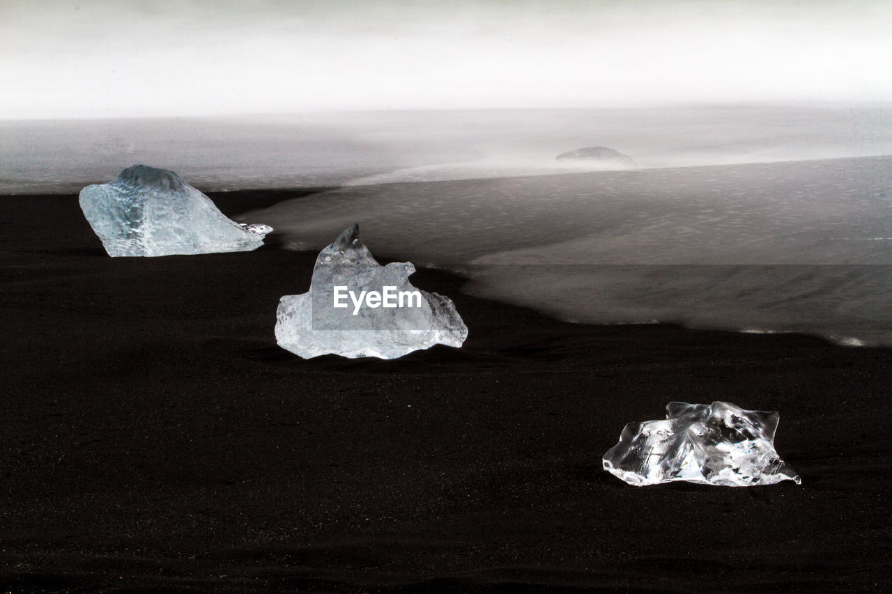 CLOSE-UP OF ICE ON ROCK AT SEA SHORE AGAINST SKY