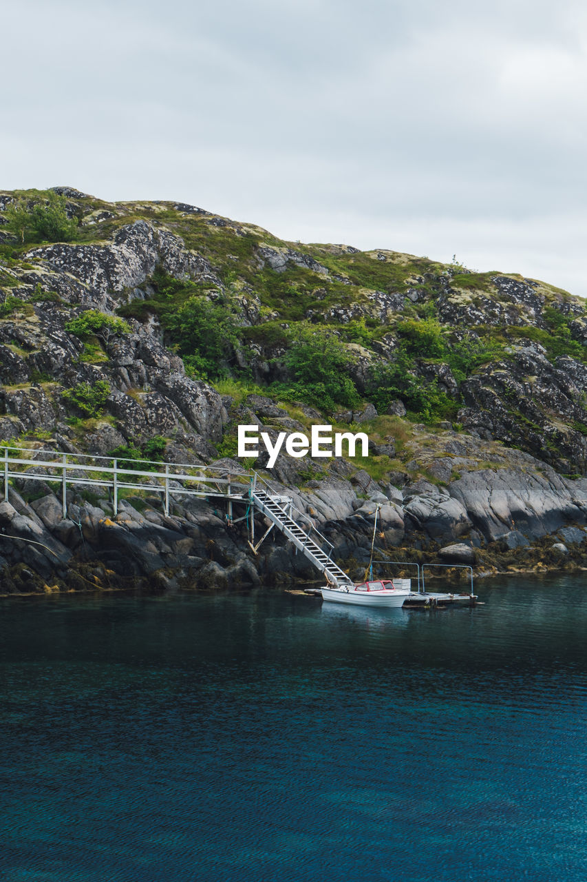 Motorboat moored near rock formation by sea against sky
