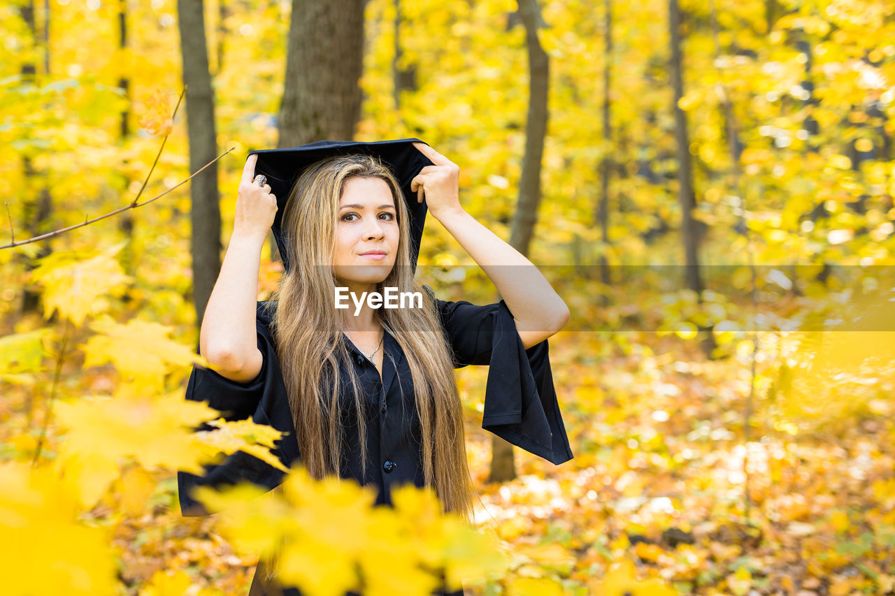 portrait of young woman wearing graduation gown standing in forest