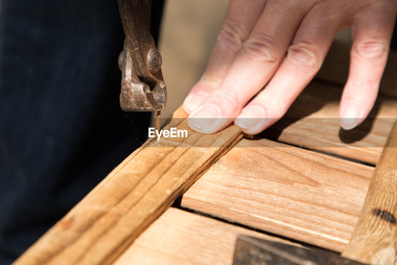 Close-up of person removing rusty nail from wood