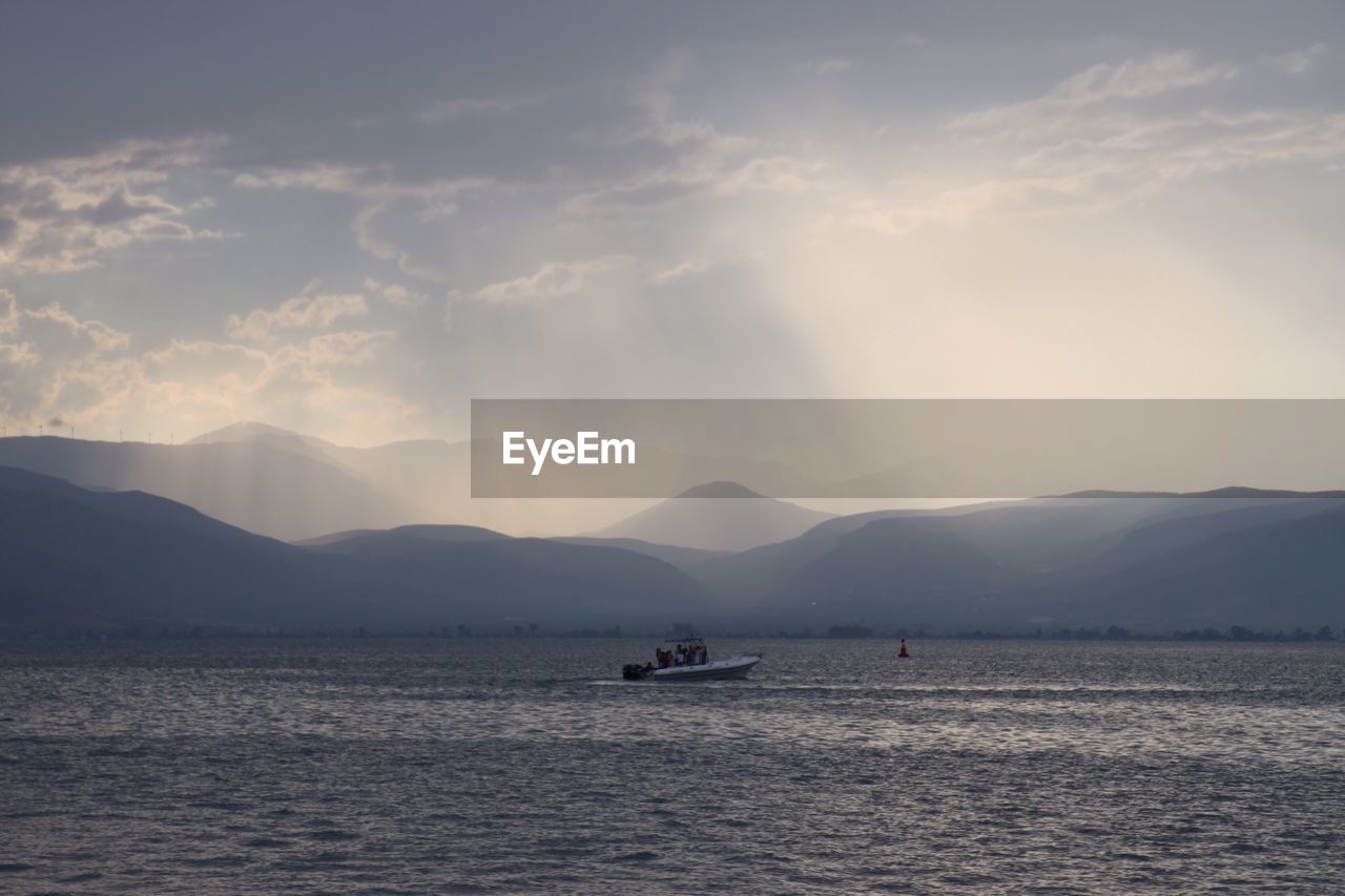 BOAT SAILING IN SEA AGAINST MOUNTAINS