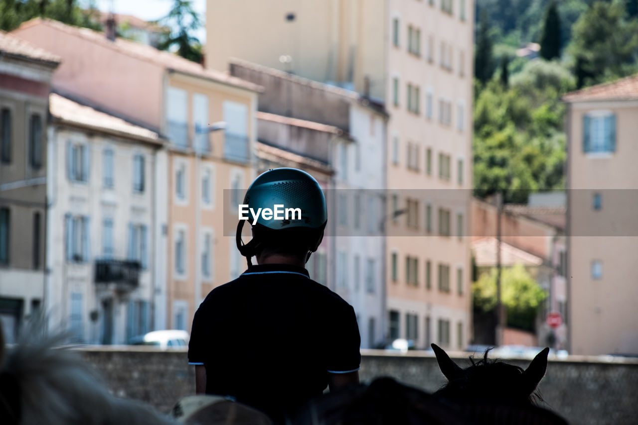 REAR VIEW PORTRAIT OF MAN STANDING ON STREET AGAINST BUILDINGS