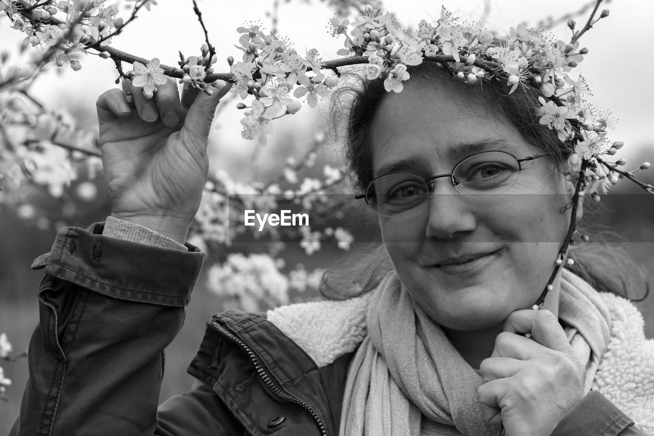 Portrait of smiling woman holding flowers on tree