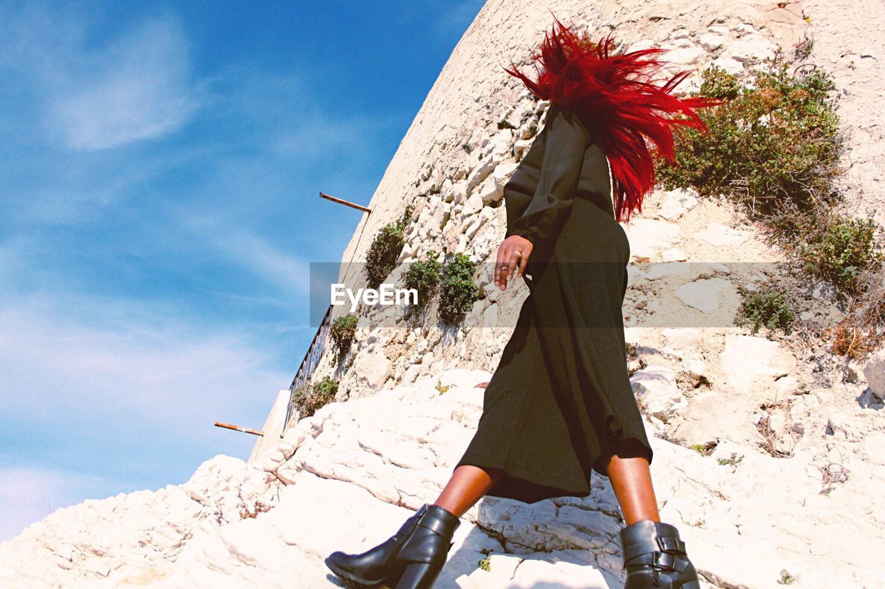 Low angle view of woman walking by wall against clear sky
