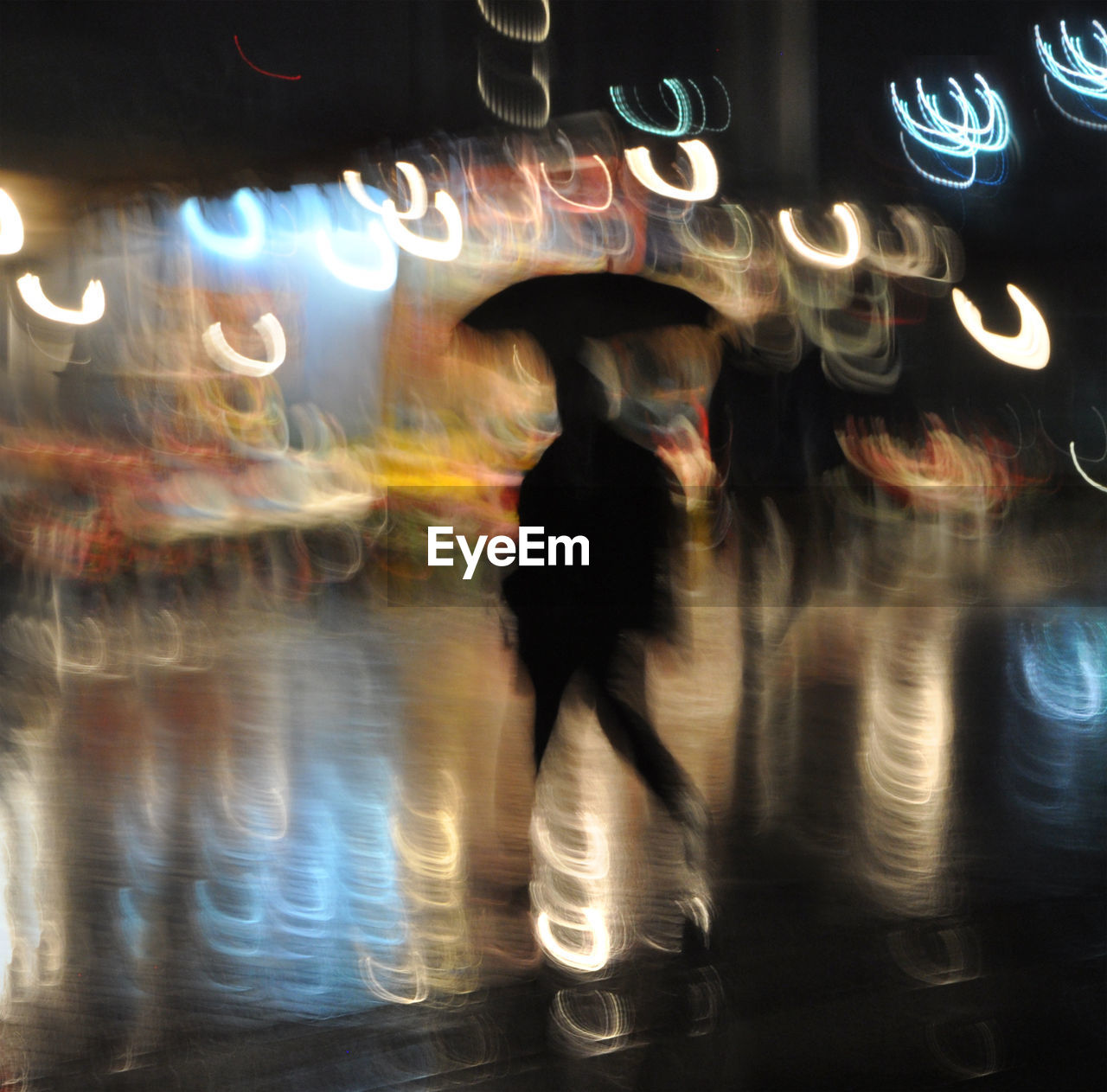 BLURRED MOTION OF PEOPLE WALKING ON ILLUMINATED STREET