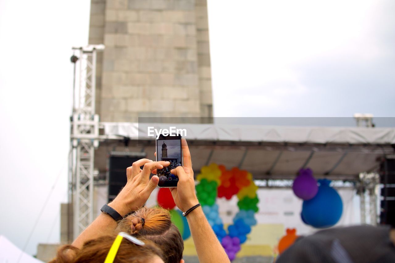 MAN PHOTOGRAPHING WITH MOBILE PHONE WHILE STANDING ON CAMERA