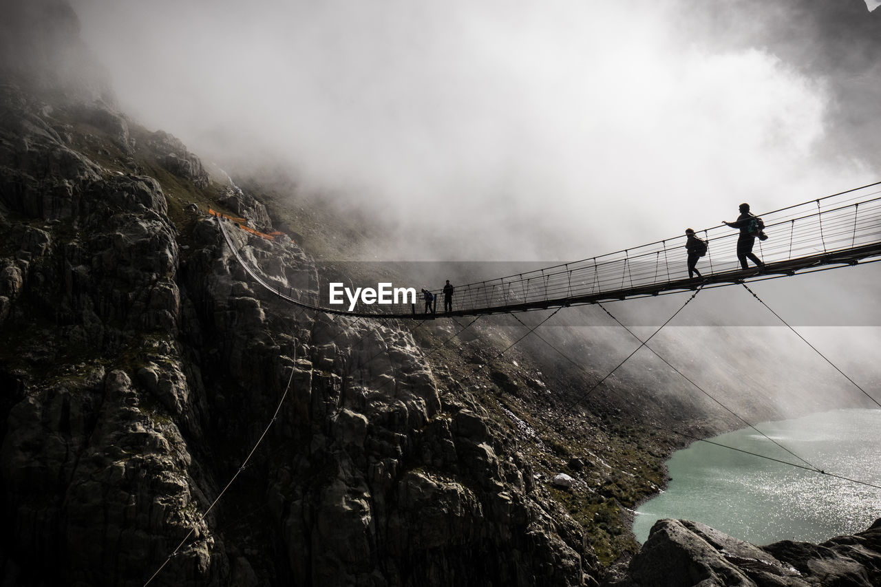 Low angle view of people on footbridge against mountains