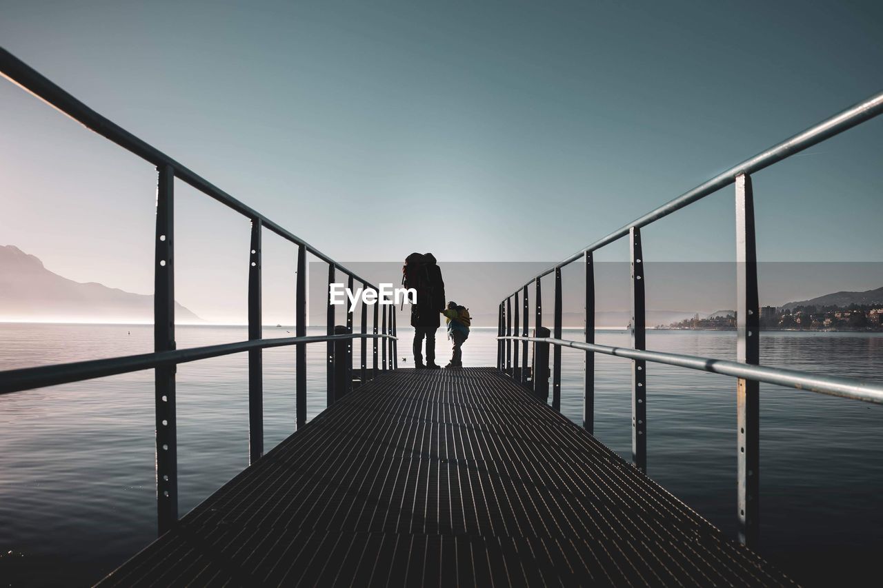 REAR VIEW OF MAN STANDING ON RAILING AGAINST SEA