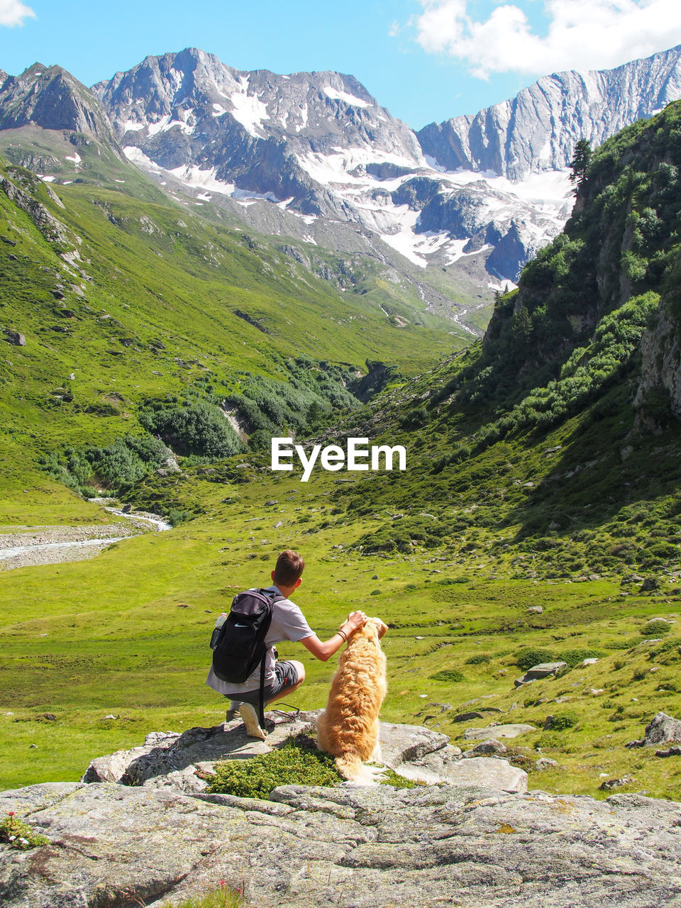 Rear view of teenage boy with dog against mountains on rock