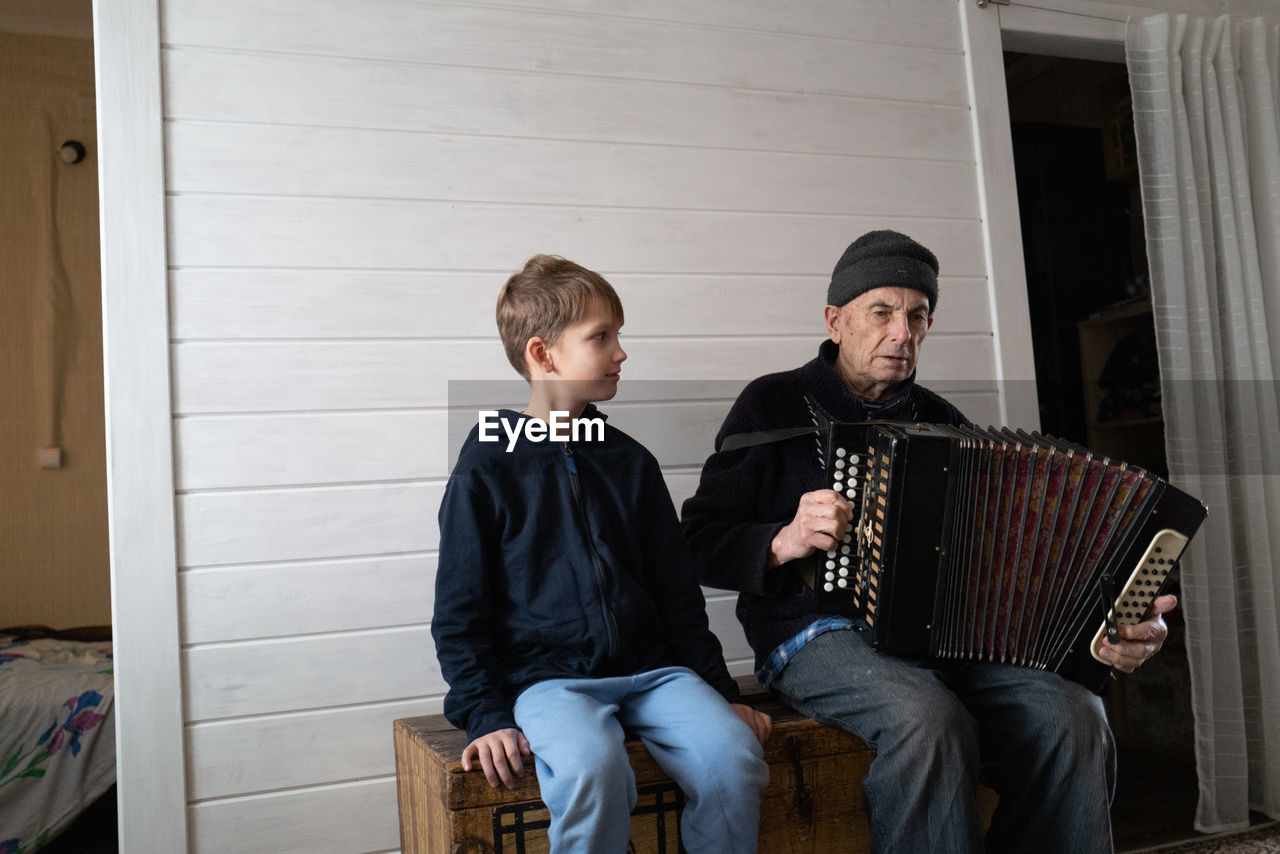 Grand father playing harmonica while sitting with grandson