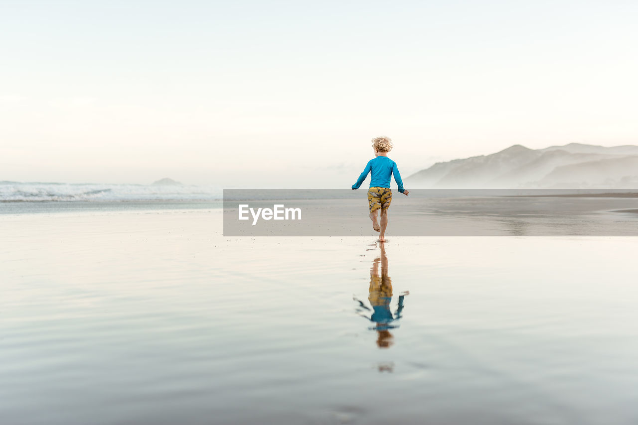 Toddler boy running on a beach with reflection